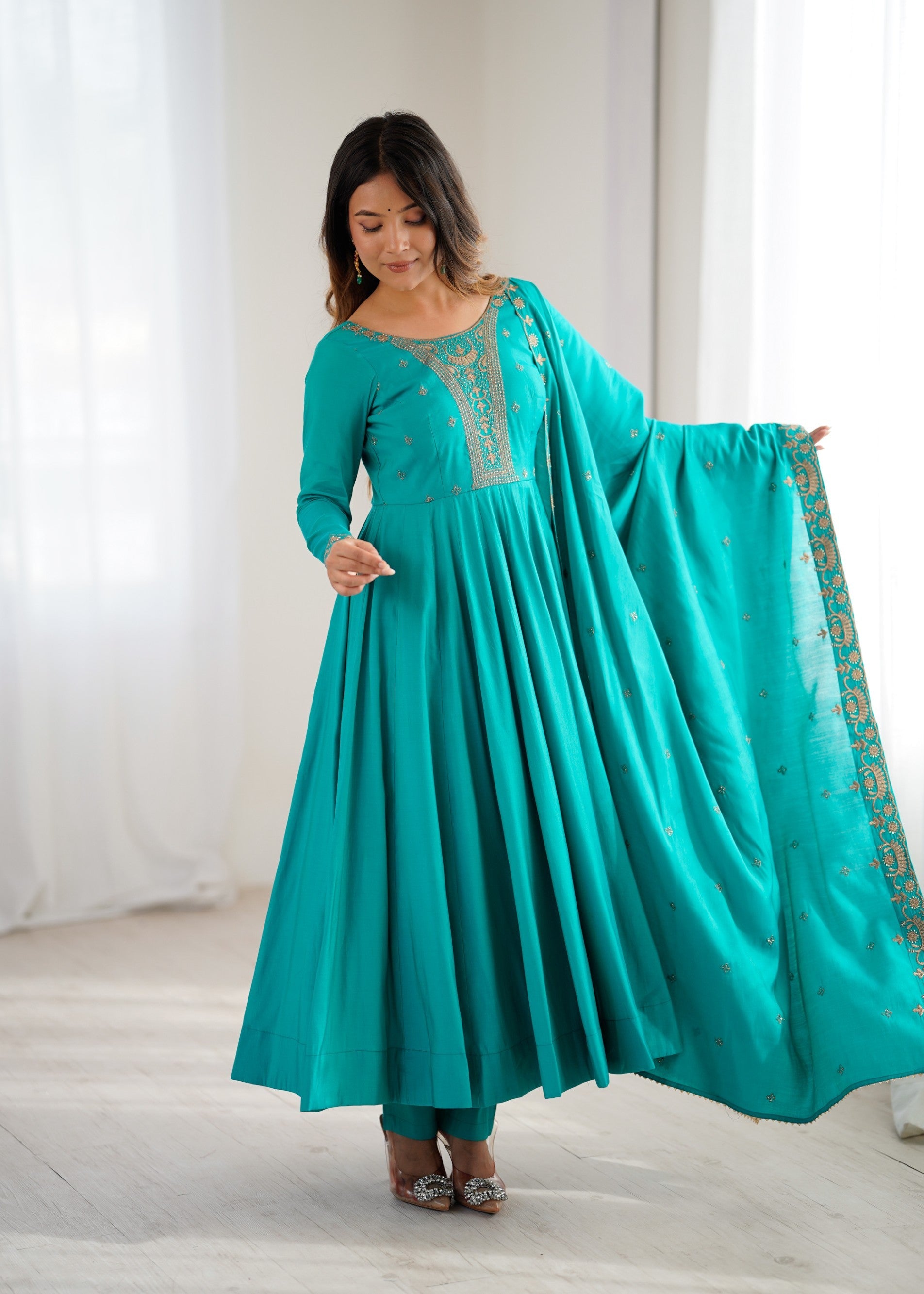 Woman wearing a teal and gold Roman Shimmer Silk Anarkali gown with intricate bead handwork and dupatta