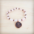 Rose Quartz beaded stretch bracelet featuring an antique copper-tone circular cross charm on a light wooden background