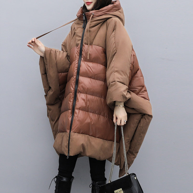 A woman wearing a thickened brown cloak-style jacket with a bat-sleeve silhouette, featuring a hood and front zipper.