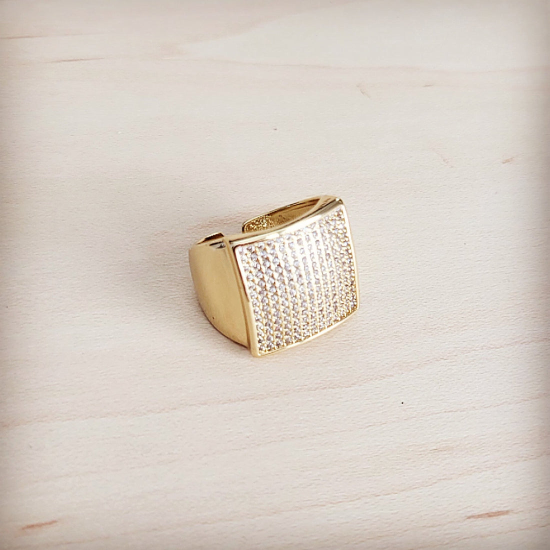 Gold-tone square ring with pave clear crystal stones and adjustable open back band on a light wooden background