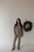 Woman wearing a bamboo long-sleeve button-up lounge set with flared pants in a black and beige vertical stripe pattern.
