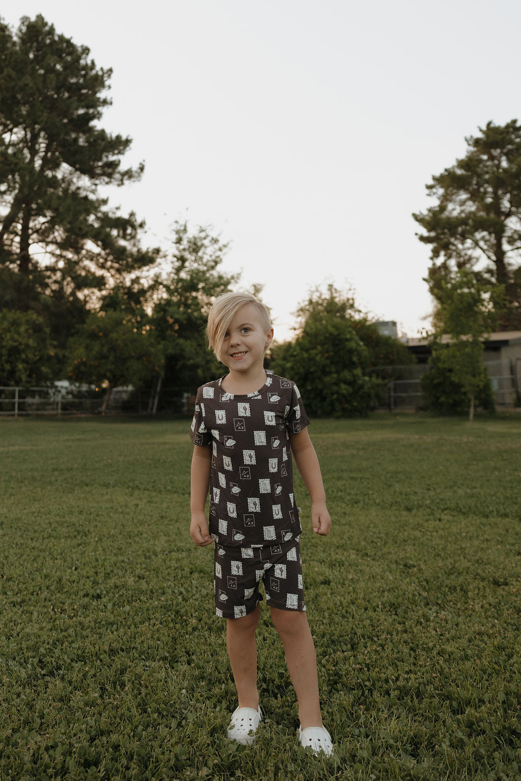 Child wearing brown bamboo short set with With Love from AZ print in a park.