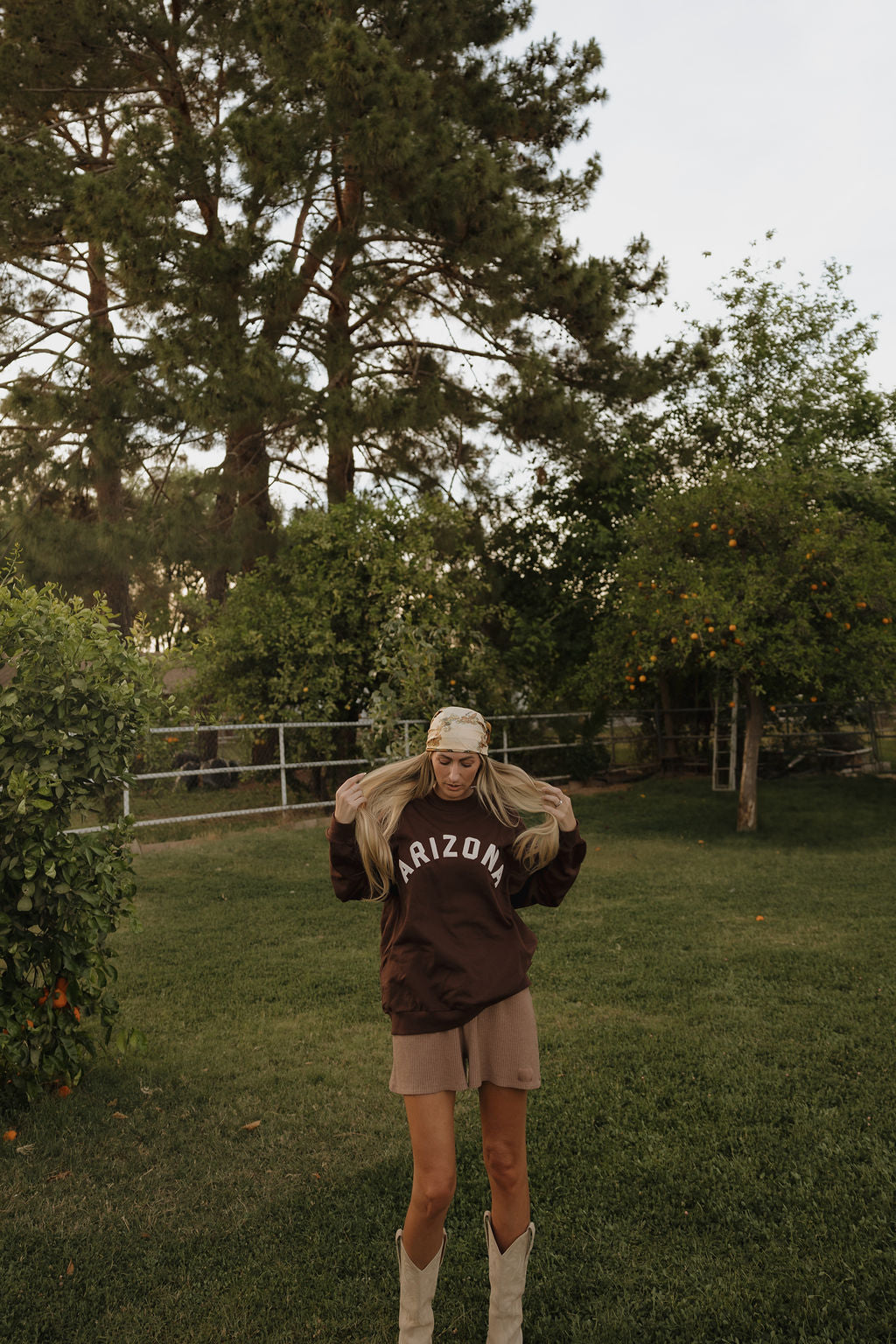 A woman wearing a brown oversized crewneck sweatshirt with 'ARIZONA' text, featuring a detail graphic on the sleeve.
