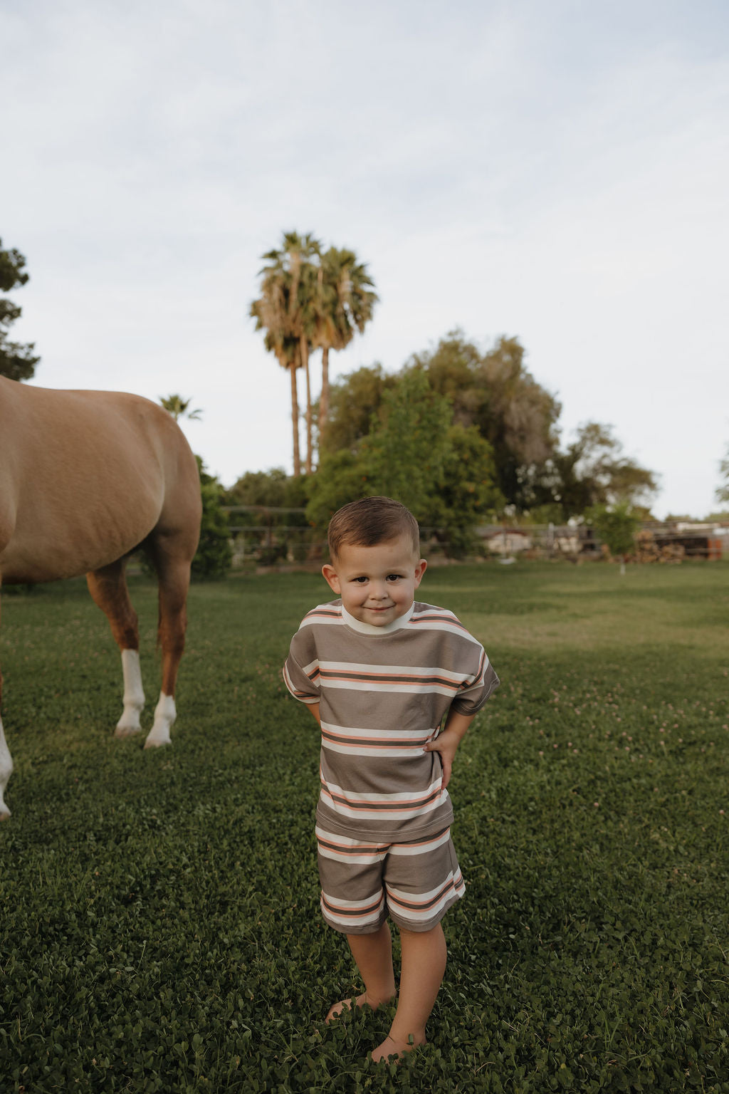 Young child wearing a comfortable Sedona Stripe cotton t-shirt and shorts set while standing outside in a grassy field.