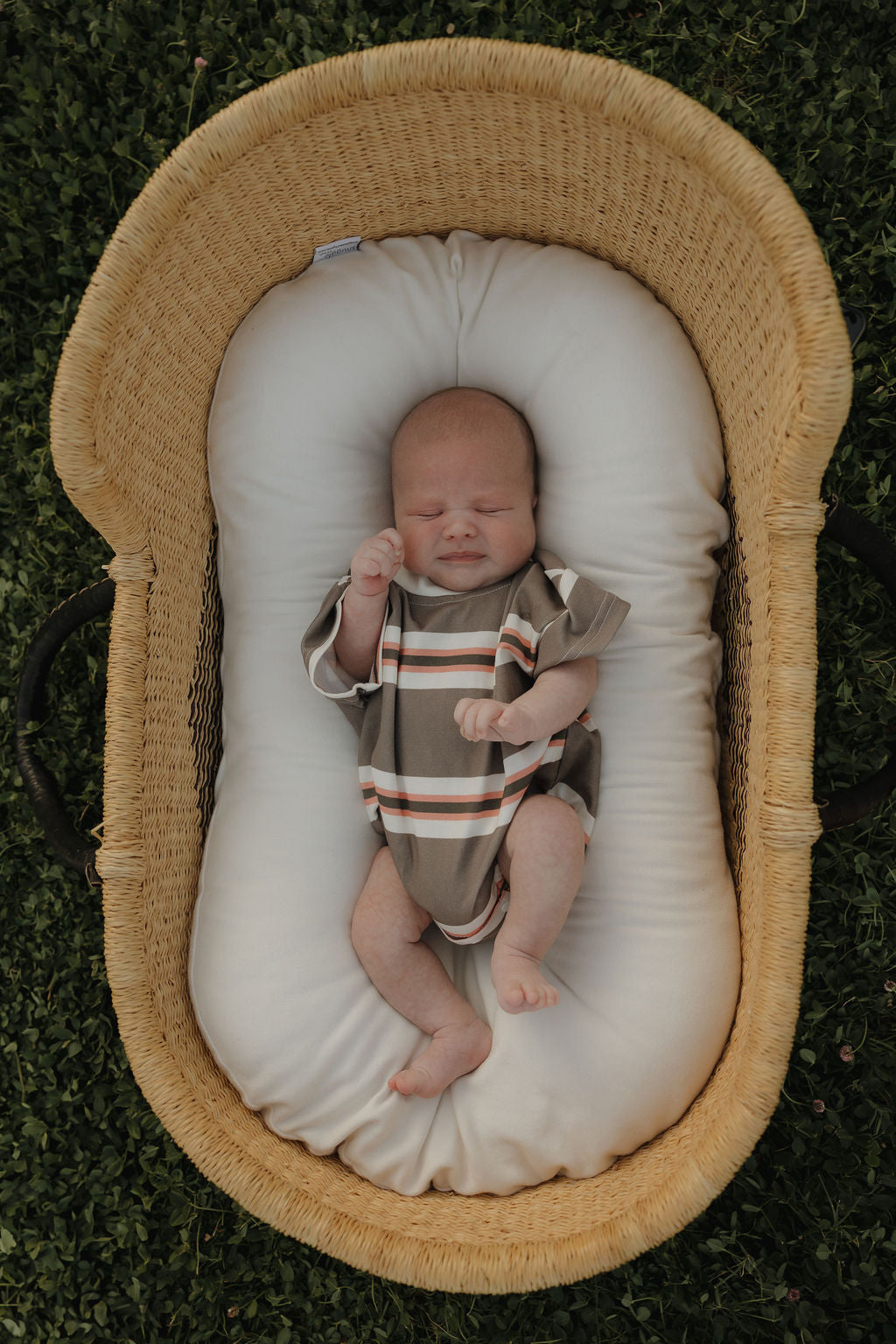 Baby wearing a Sedona Stripe short sleeve romper while resting in a woven basket.