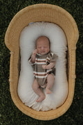 Baby wearing a Sedona Stripe short sleeve romper while resting in a woven basket.