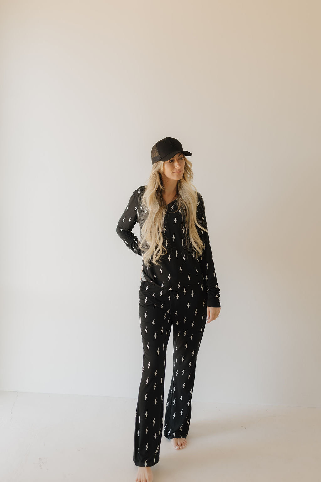 Woman wearing a black long-sleeve pajama set with a white lightning bolt pattern, standing in a studio setting.