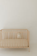 Flora print muslin crib sheet in soft peach tone displayed on a wooden crib