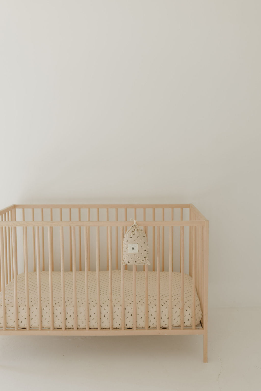 Flora print muslin crib sheet in soft peach tone displayed on a wooden crib