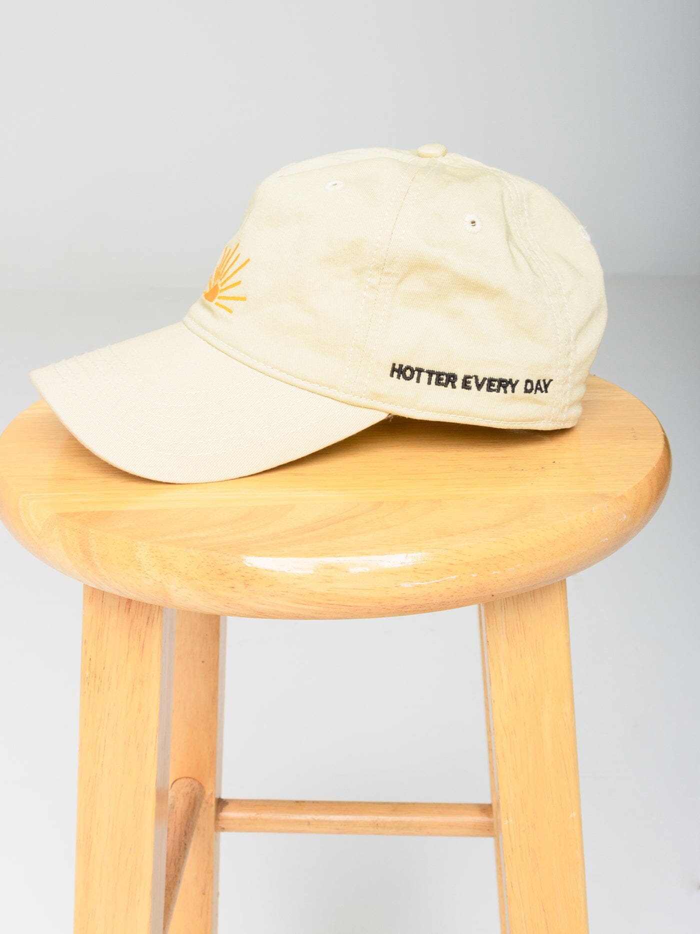 Hotter Every Day baseball hat with front sunrise embroidery and side text in a lifestyle setting