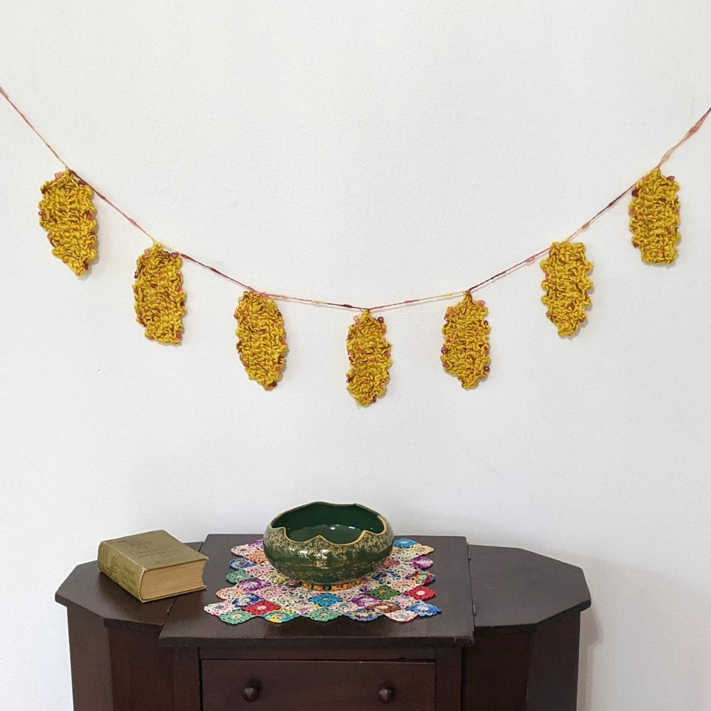 Close up of handmade festive fall leaves in yellow, rust, and brown hanging on a string for rustic bohemian home decor