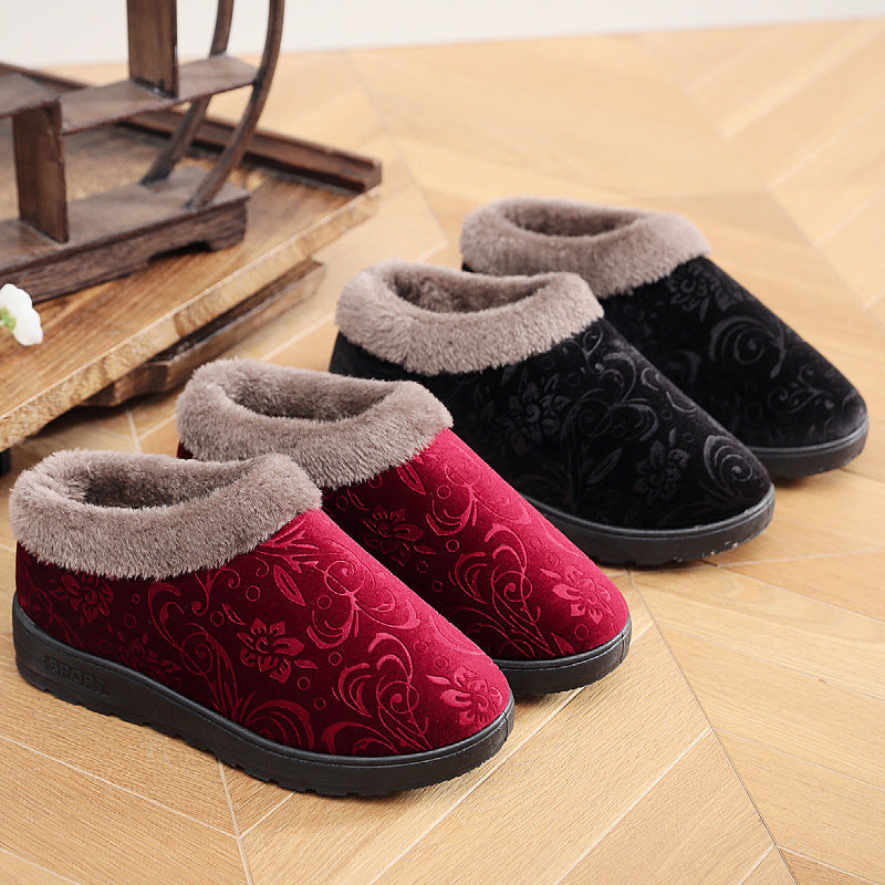 Close up of plush velvet women's slippers in burgundy and black with soft faux-fur trim on a soft surface.