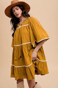 A bohemian tiered dress with tassel accents on the tie neck and contrast trim
