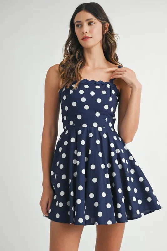 Woman wearing a navy blue polka dot mini dress with ricrac trim straps