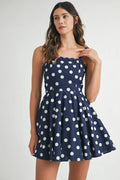 Woman wearing a navy blue polka dot mini dress with ricrac trim straps