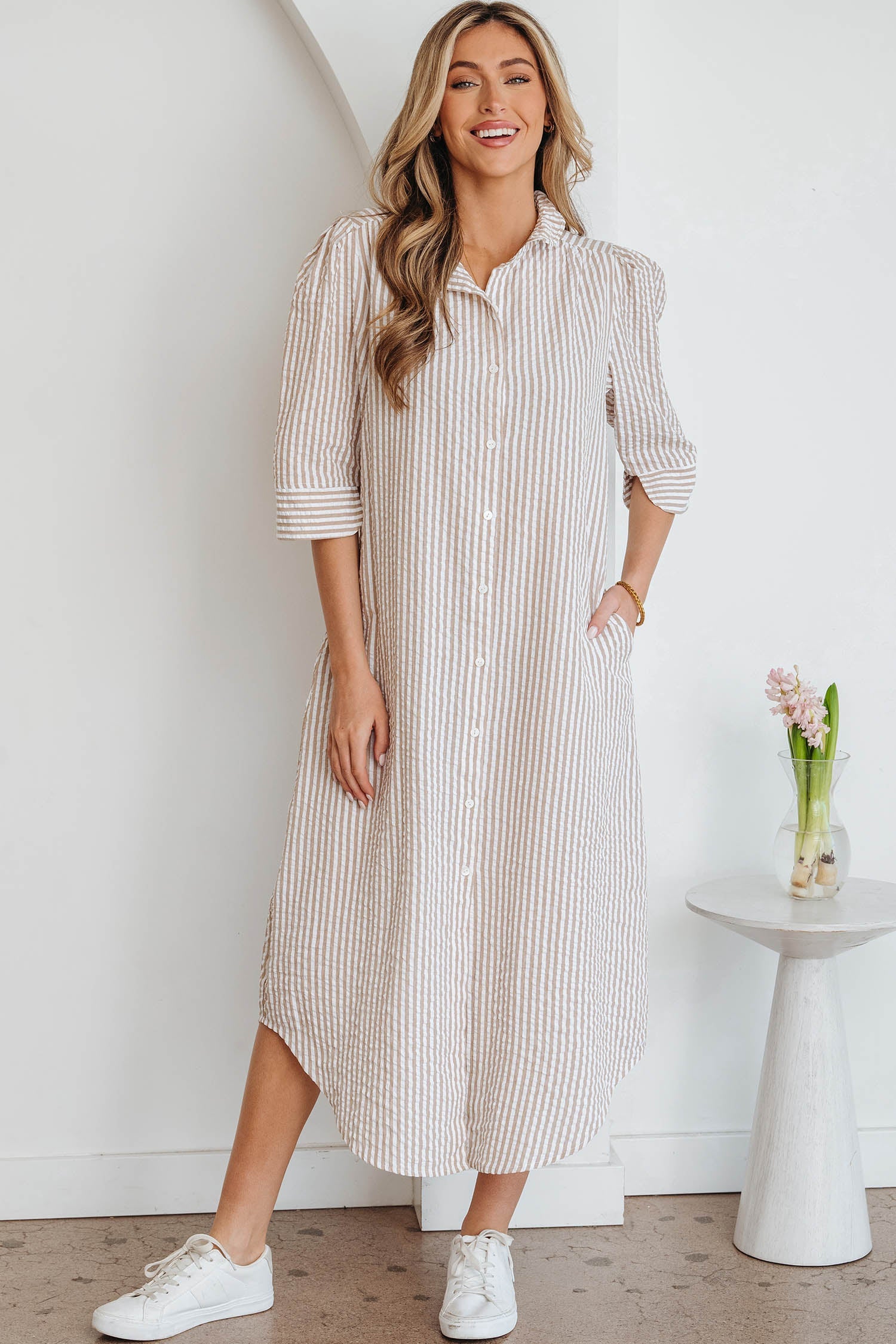 A woman wearing a tan and white striped half-sleeve shirt dress with a collar and buttons, styled with white sneakers.