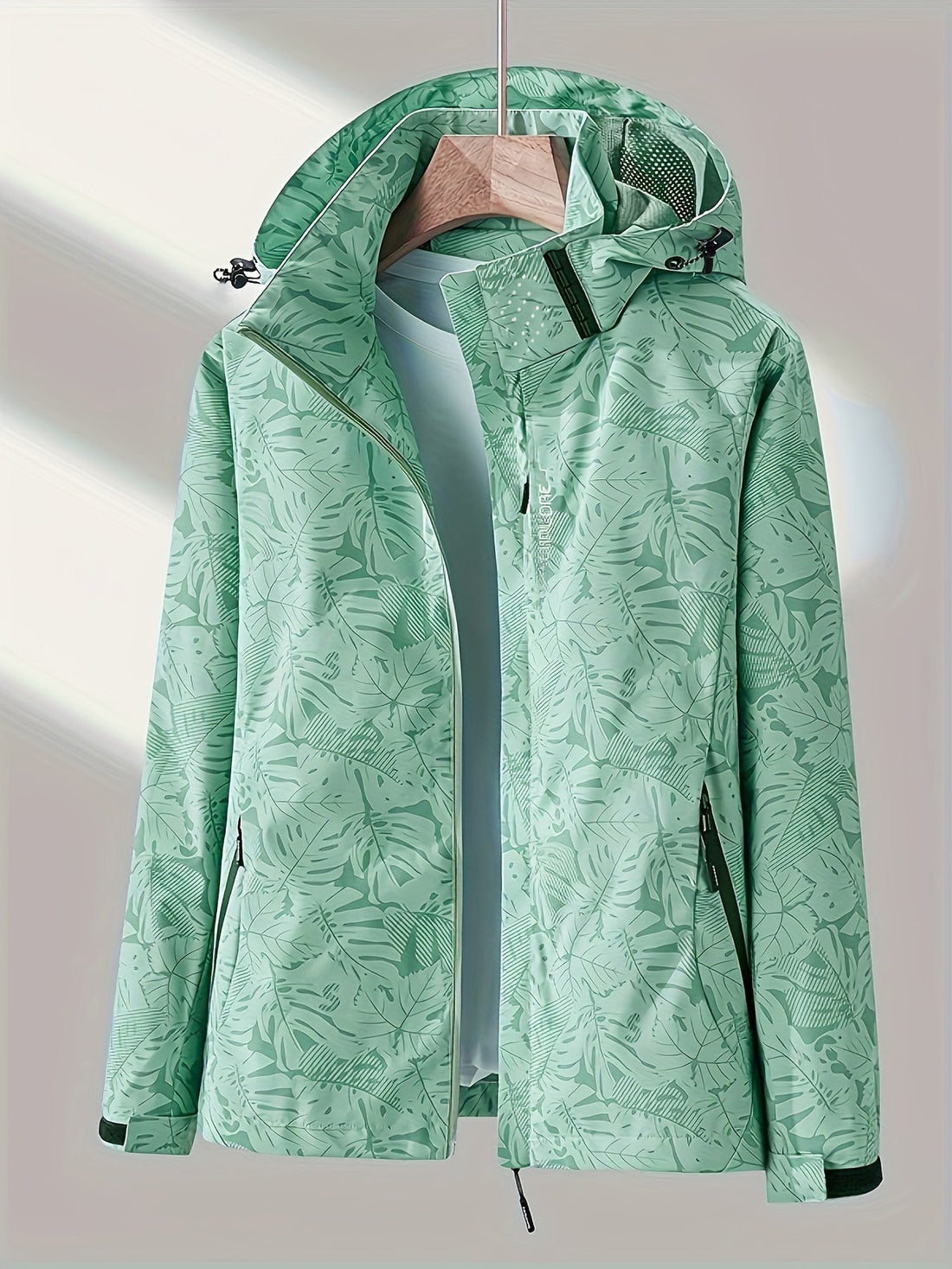 Women's windproof jacket with tropical leaf print in light green and black options on a hanger.
