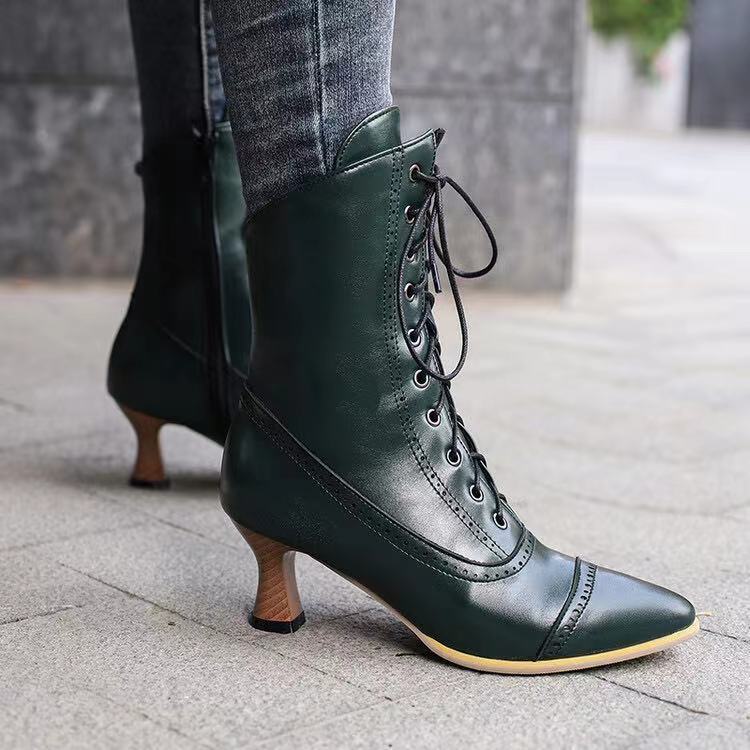 A pair of women's dark green mid-calf boots with a wine glass shaped heel and lace-up front detail.