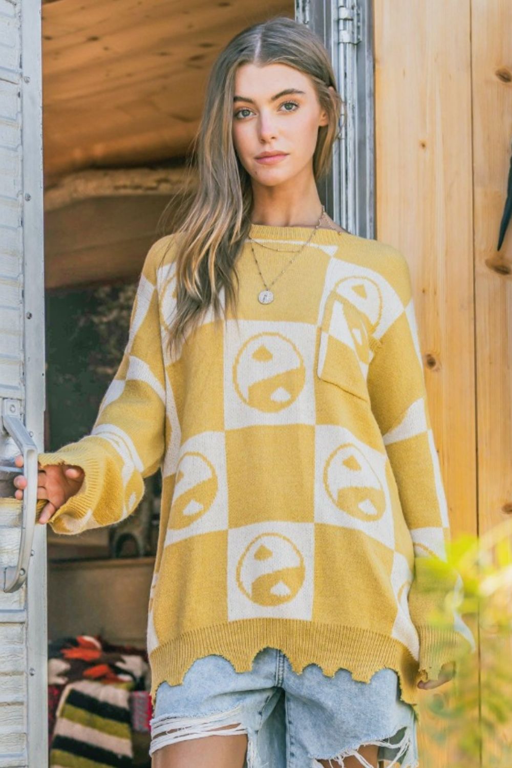 Model wearing a yellow and cream checkerboard sweater with yin yang symbols and distressed hem details