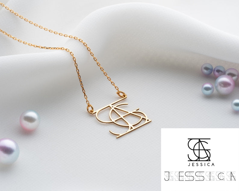 Close-up of a minimalist gold intertwined initial monogram necklace on a neutral background.