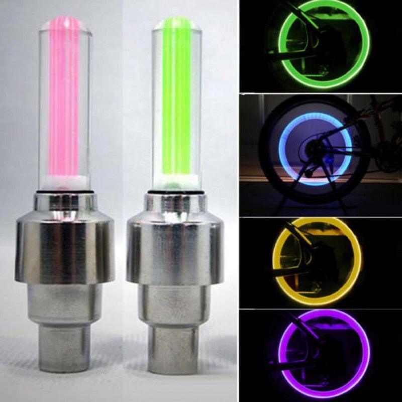 Set of two silver LED tire valve cap lights glowing in multi-color on a bicycle wheel at night.