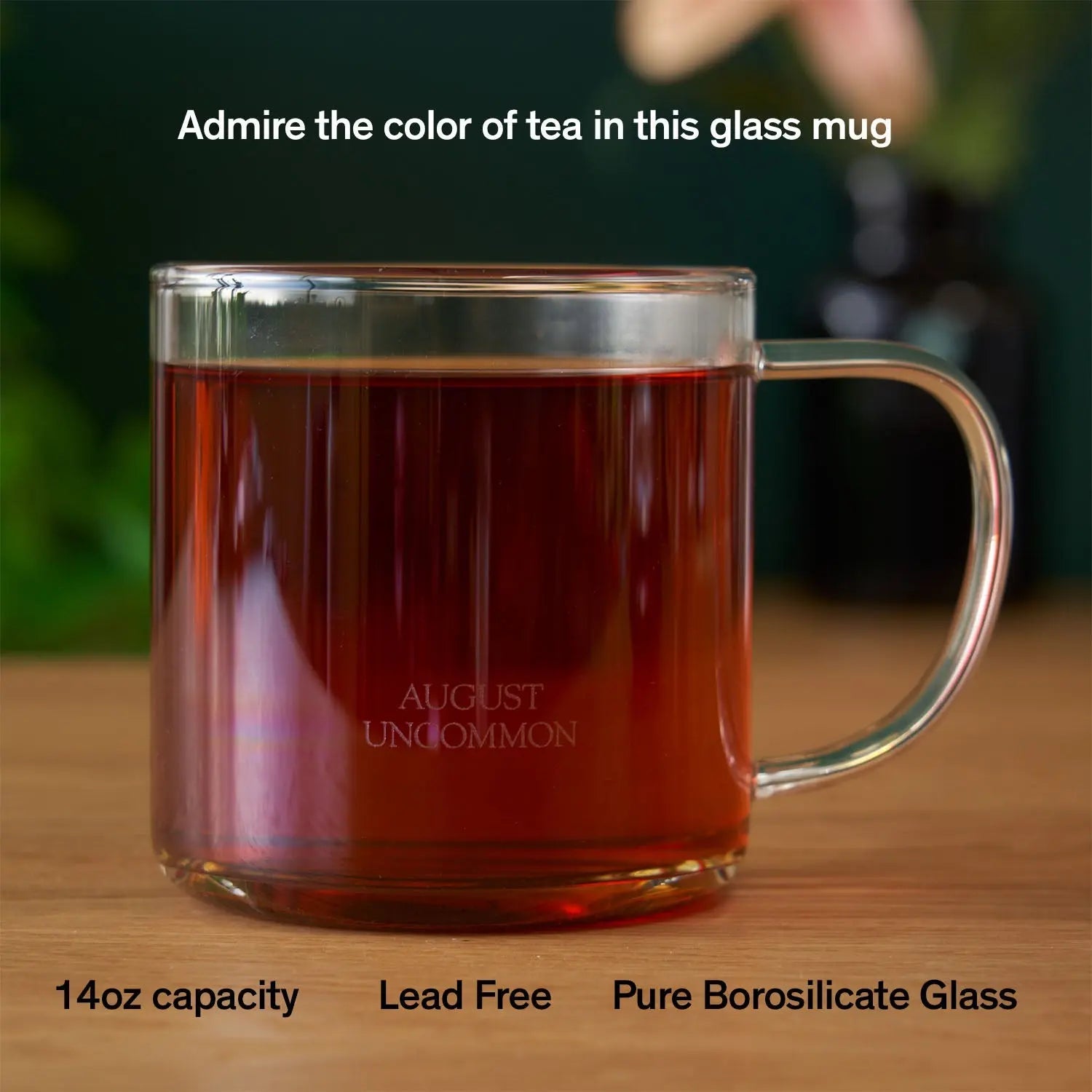 A clear, 14oz borosilicate glass tea mug sitting on a wooden surface, showing the rich color of tea inside.