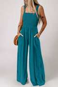 Peacock blue sleeveless jumpsuit featuring a smocked square neckline and side pockets.