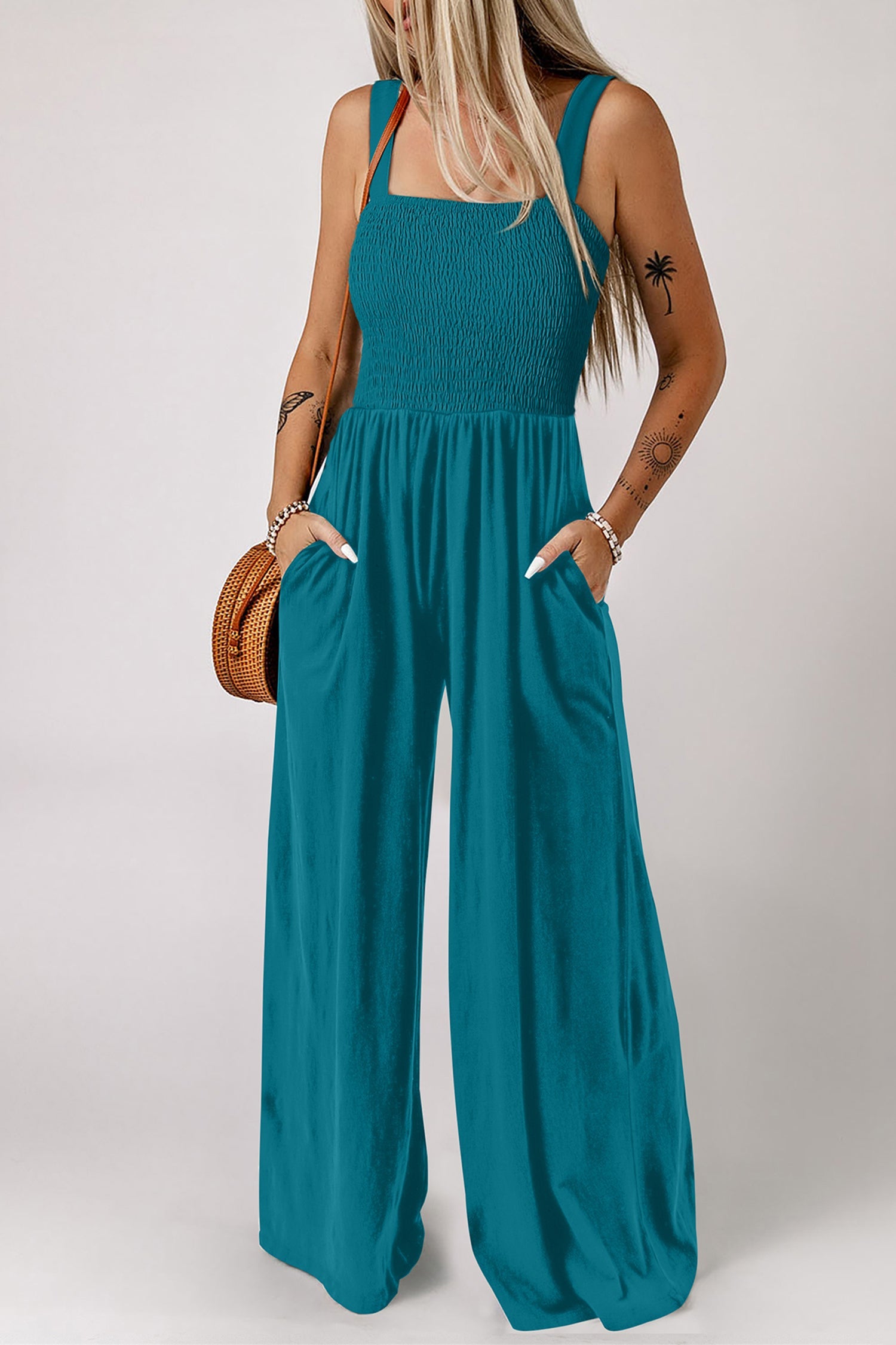 Peacock blue sleeveless jumpsuit featuring a smocked square neckline and side pockets.