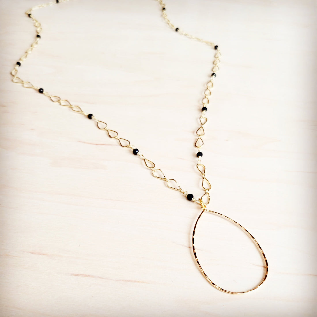 Gold-tone infinity link chain necklace with black faceted bead accents and a teardrop pendant