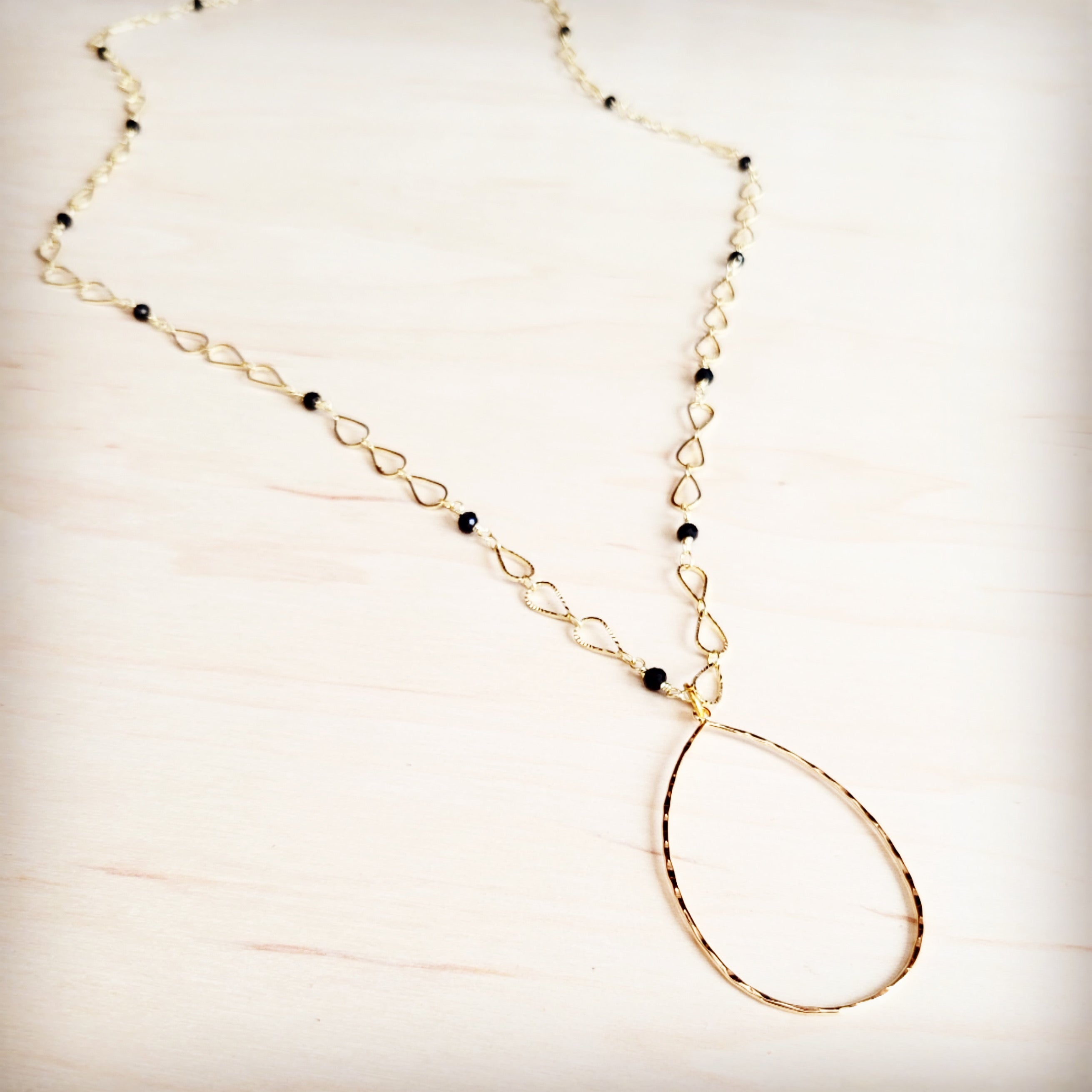 Gold-tone infinity link chain necklace with black faceted bead accents and a teardrop pendant
