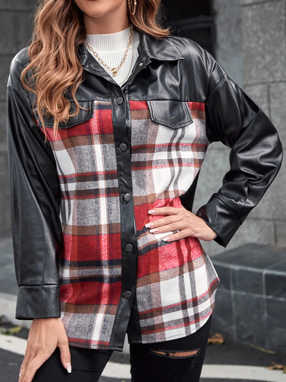 Woman wearing a red, white, and brown plaid body with black faux leather sleeves shirt jacket, styled casually with a white top and black pants.