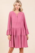 Woman wearing a mauve tiered A-line mini dress with long flare sleeves and a notched neckline.