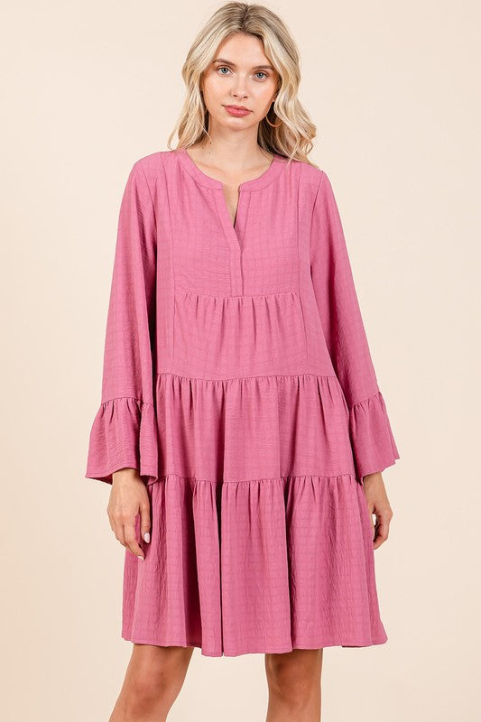 Woman wearing a mauve tiered A-line mini dress with long flare sleeves and a notched neckline.