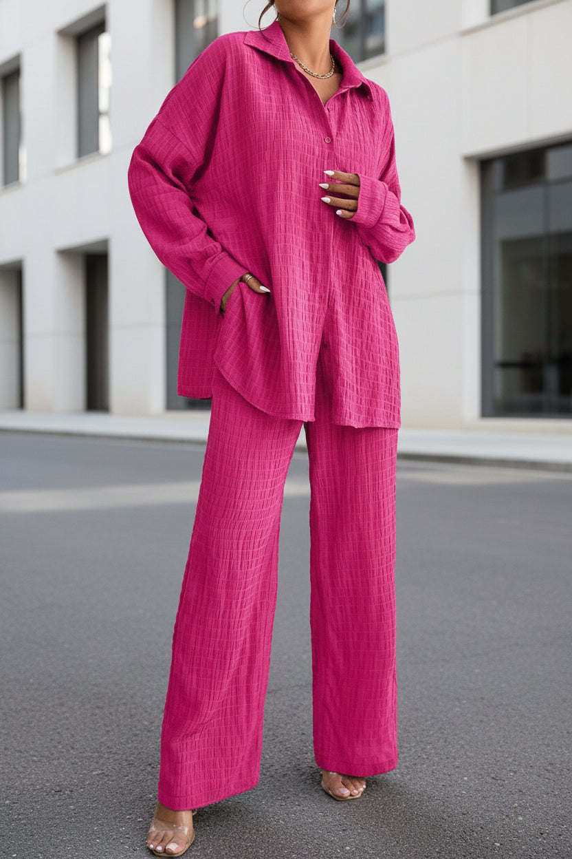 Woman wearing a matching pleated long sleeve button-down shirt and wide-leg trousers set in pink and olive green.