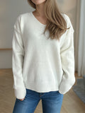 Woman wearing a white V-neck long sleeve sweater with dropped shoulders, paired with blue jeans.