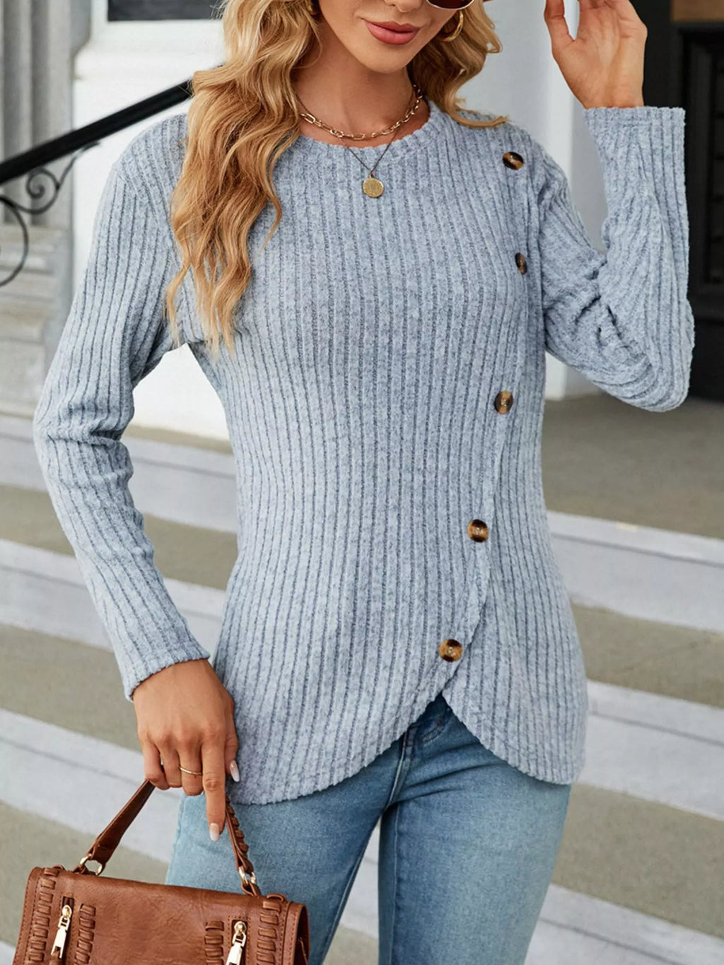 Close-up of a model wearing a light blue vertical ribbed knit long sleeve top with decorative buttons on the side.