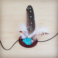 Close-up of a sunrise regalite stone and feather hat band on a genuine leather strap.