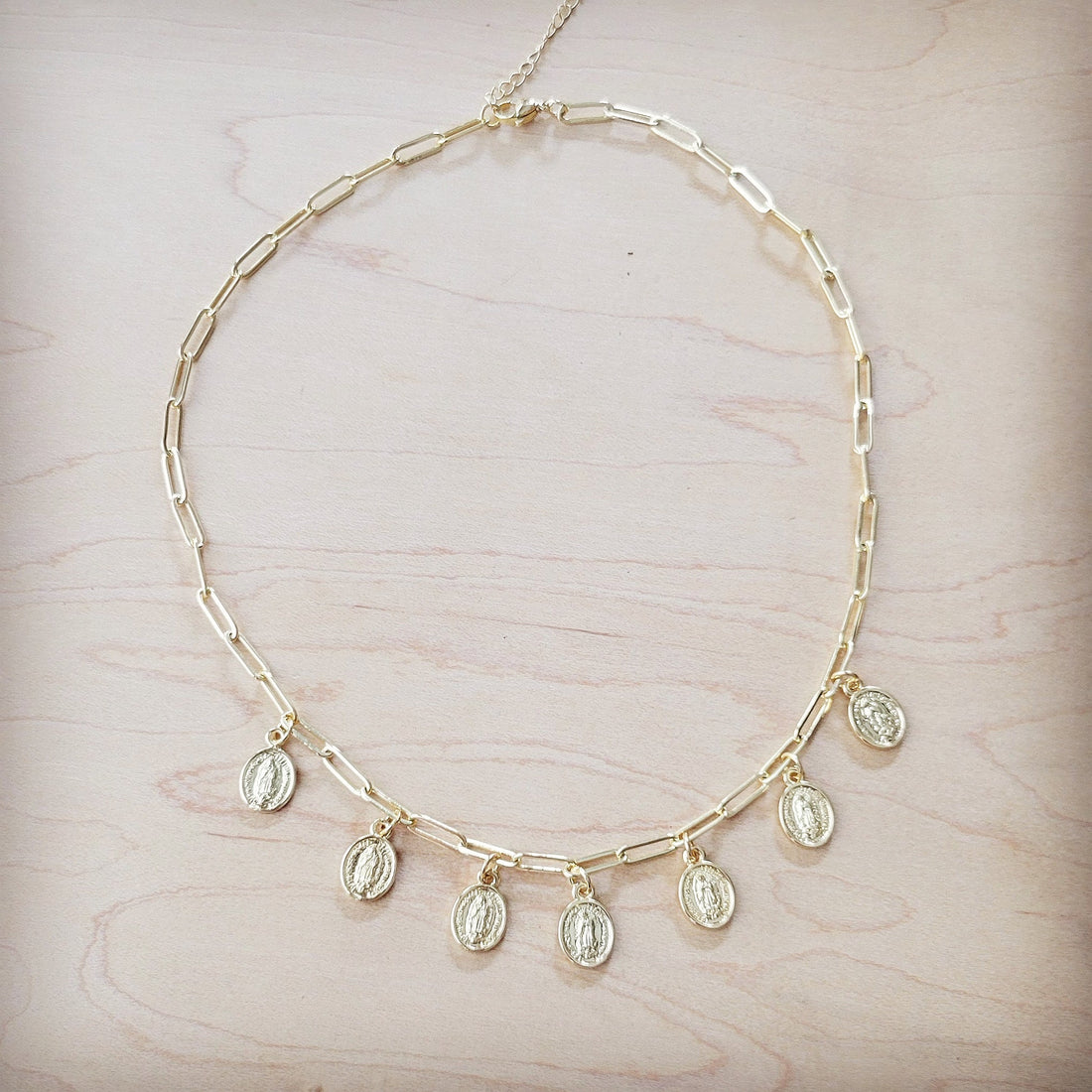 A gold-toned paperclip chain necklace with multiple small hanging coin pendants on a light wooden background.