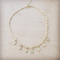 A gold-toned paperclip chain necklace with multiple small hanging coin pendants on a light wooden background.