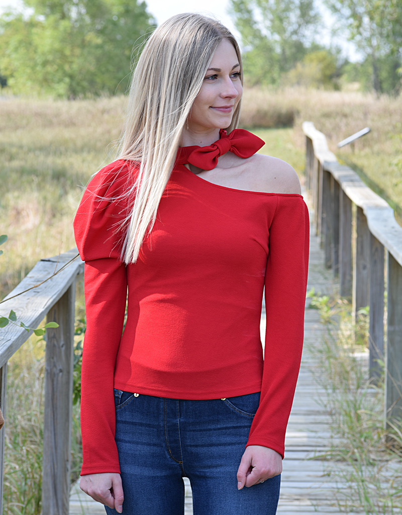 A woman wearing a vibrant red cold-shoulder halter blouse in a romantic, modern party setting.