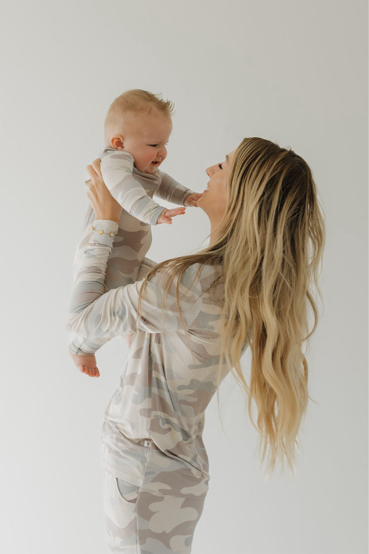 Woman wearing a long-sleeve button-front bamboo pajama top and flared pants in a beige, taupe, and grey camo print.