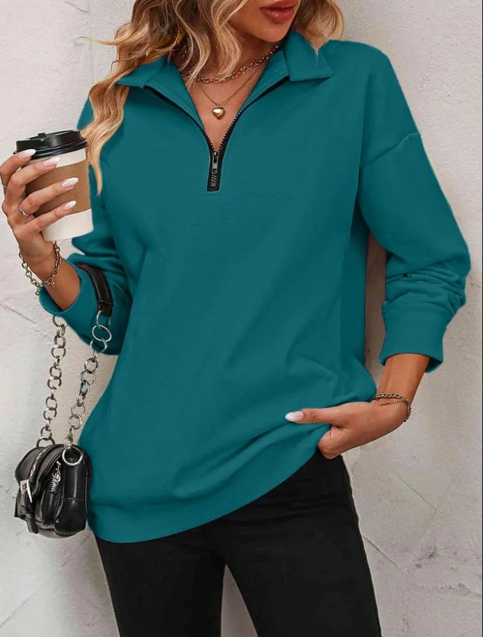 Woman wearing a teal long-sleeve top with a zipper, holding a coffee cup and a black handbag.
