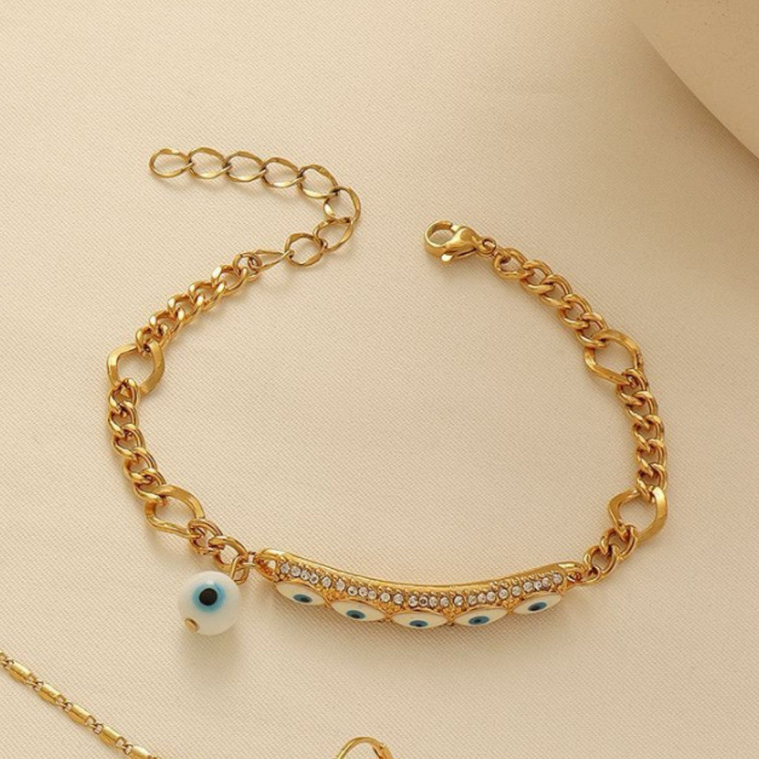 A coordinated gold-tone Evil Eye necklace, bracelet, and earring set on a display background.