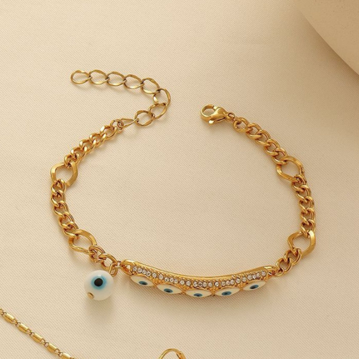 A coordinated gold-tone Evil Eye necklace, bracelet, and earring set on a display background.
