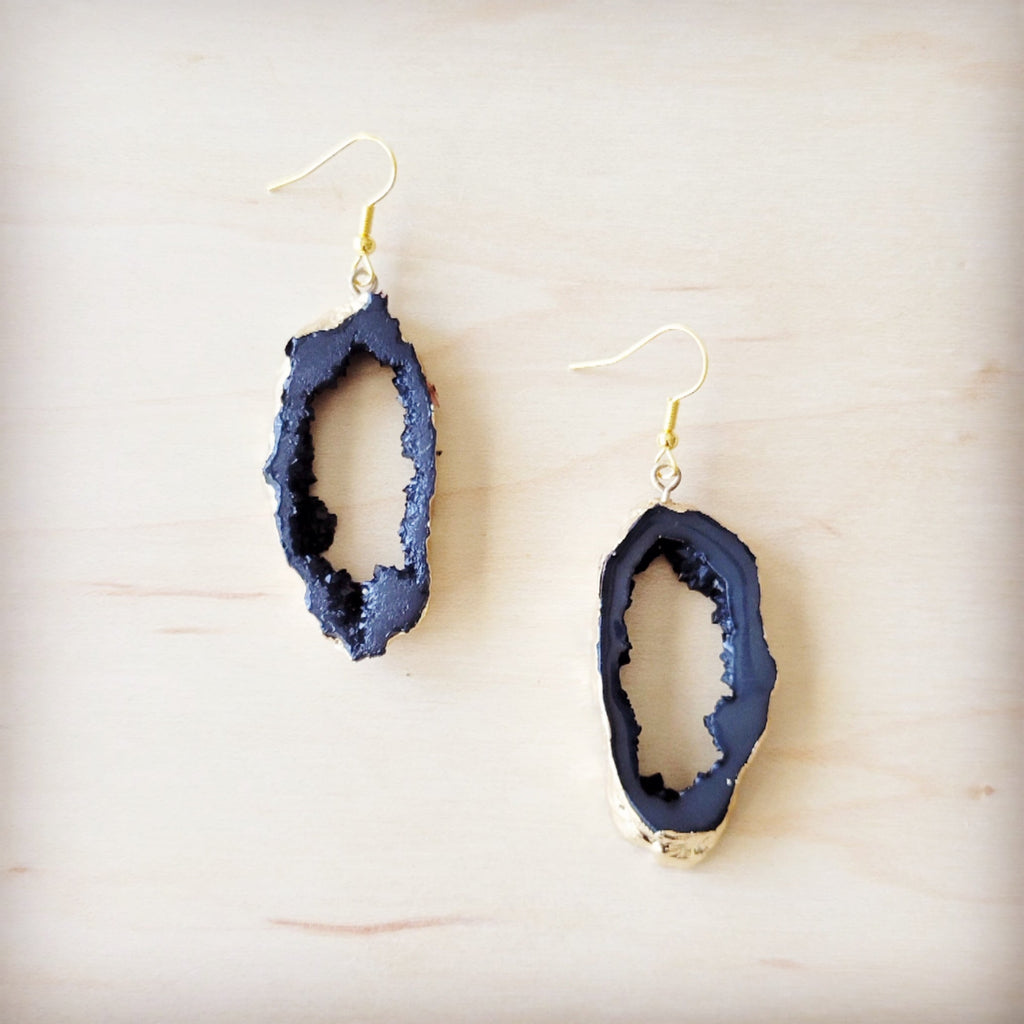 A pair of black crystalized geode dangle earrings with gold-tone edges on a light wooden background.