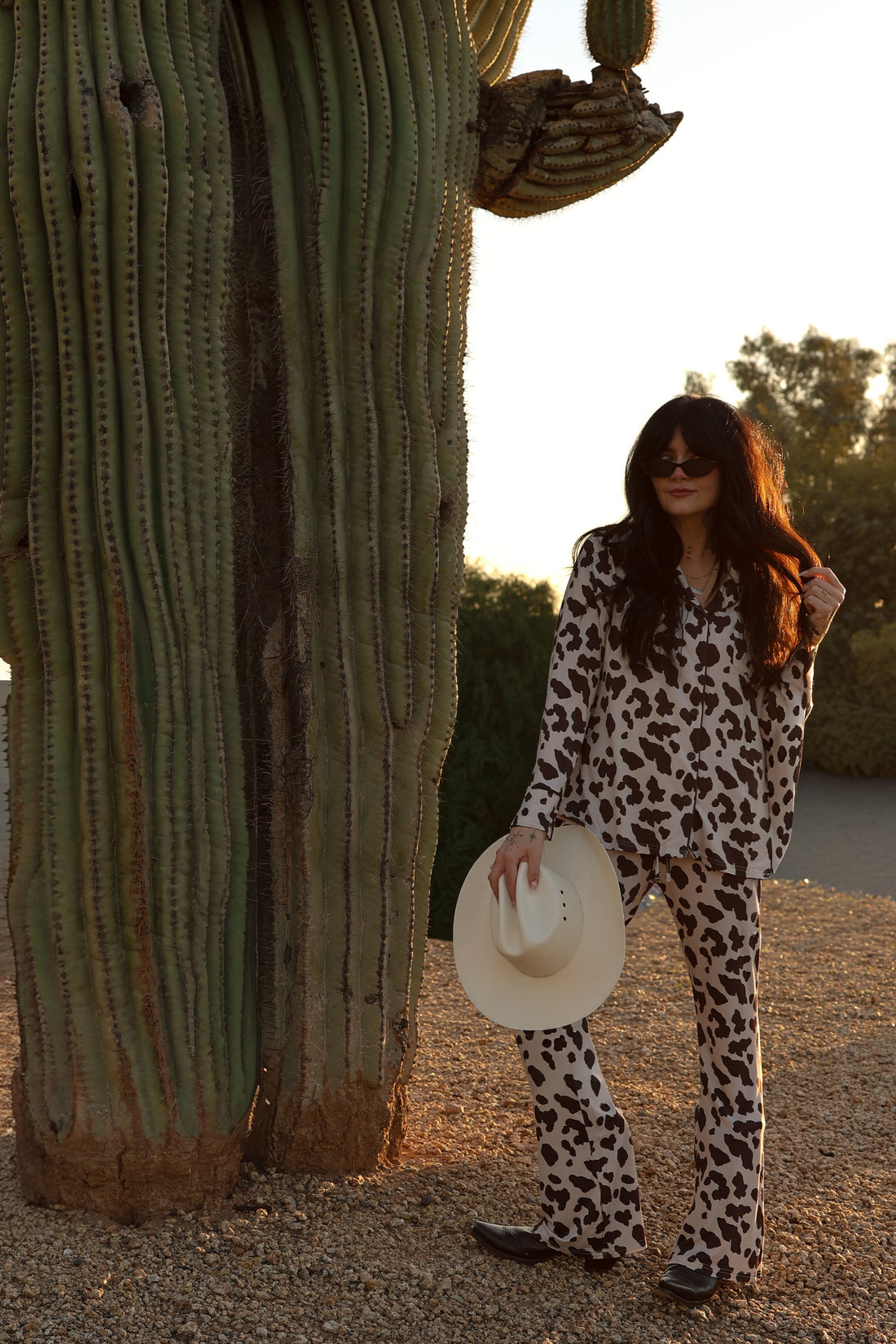 Woman wearing a cow print bamboo button-up lounge set with a collared top and flared pants in cream and brown.
