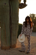 Woman wearing a cow print bamboo button-up lounge set with a collared top and flared pants in cream and brown.