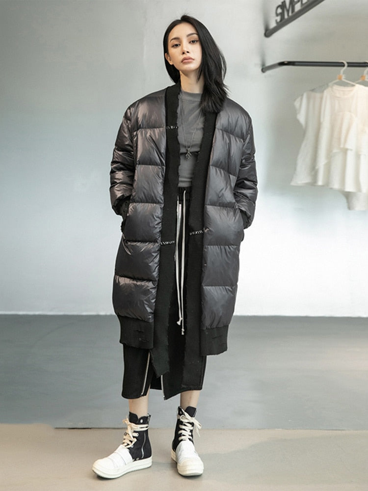 Model wearing a long black Harajuku style loose fit puffer parka jacket with white stitching details, black pants, and black and white sneakers.