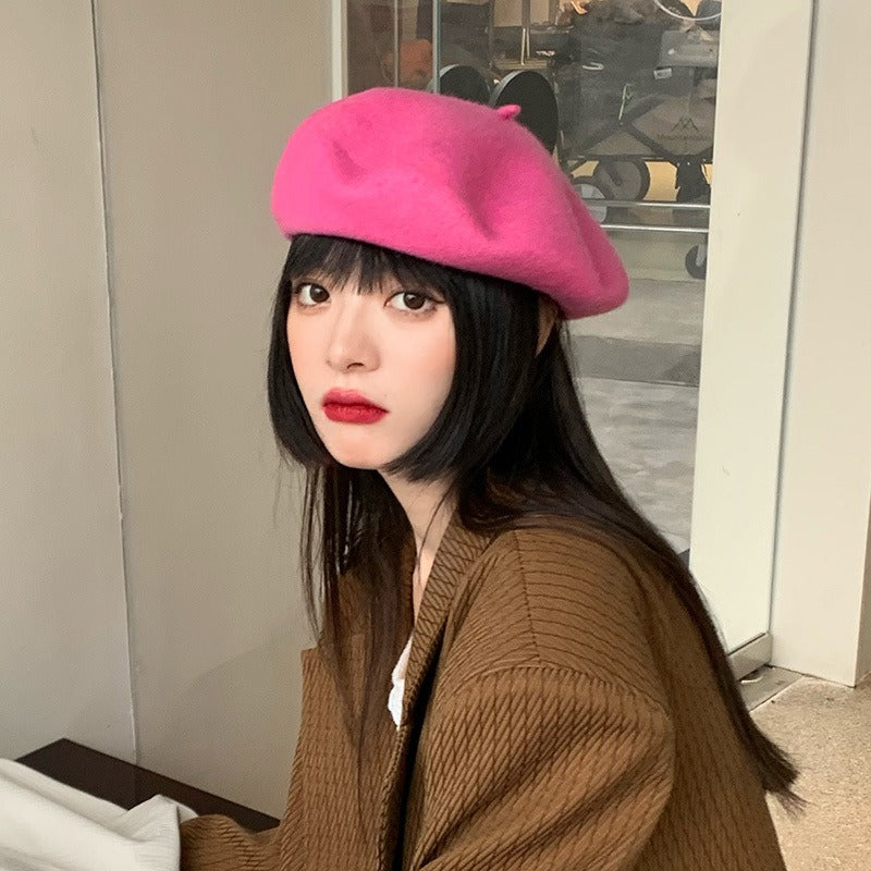 A vibrant pink wool blend beret worn by a model, and an olive green wool blend beret shown flat lay with a book, highlighting the candy-colored, retro Harajuku style.