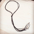 Dark brown leather lasso necklace with raw white turquoise stone accents on a wooden background
